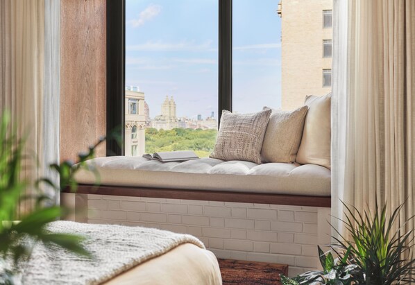 Quarto com um assento junto à janela, parede de tijolos e vista para a paisagem urbana.