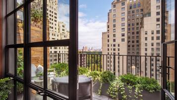 A balcony with a view of tall buildings, a potted plant, and a chair.