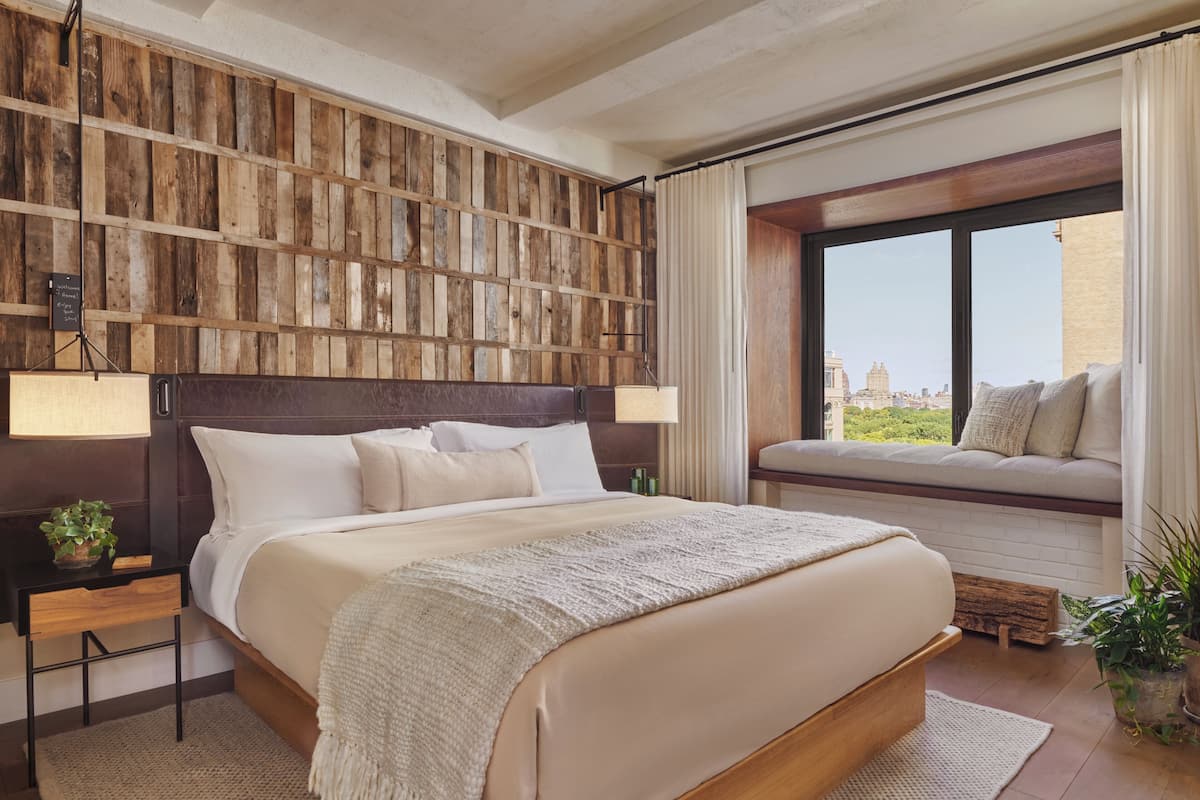 Quarto de hotel com cama grande, painel de parede de madeira, assento junto à janela e vista para a cidade.