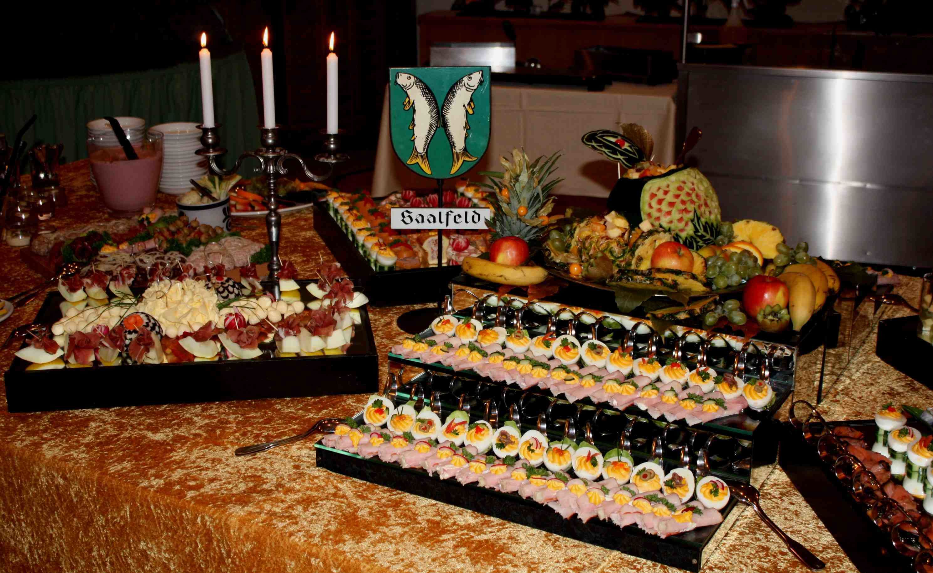 Una mesa de buffet con diversos alimentos, incluyendo un cartel que dice 'Saalfeld'.