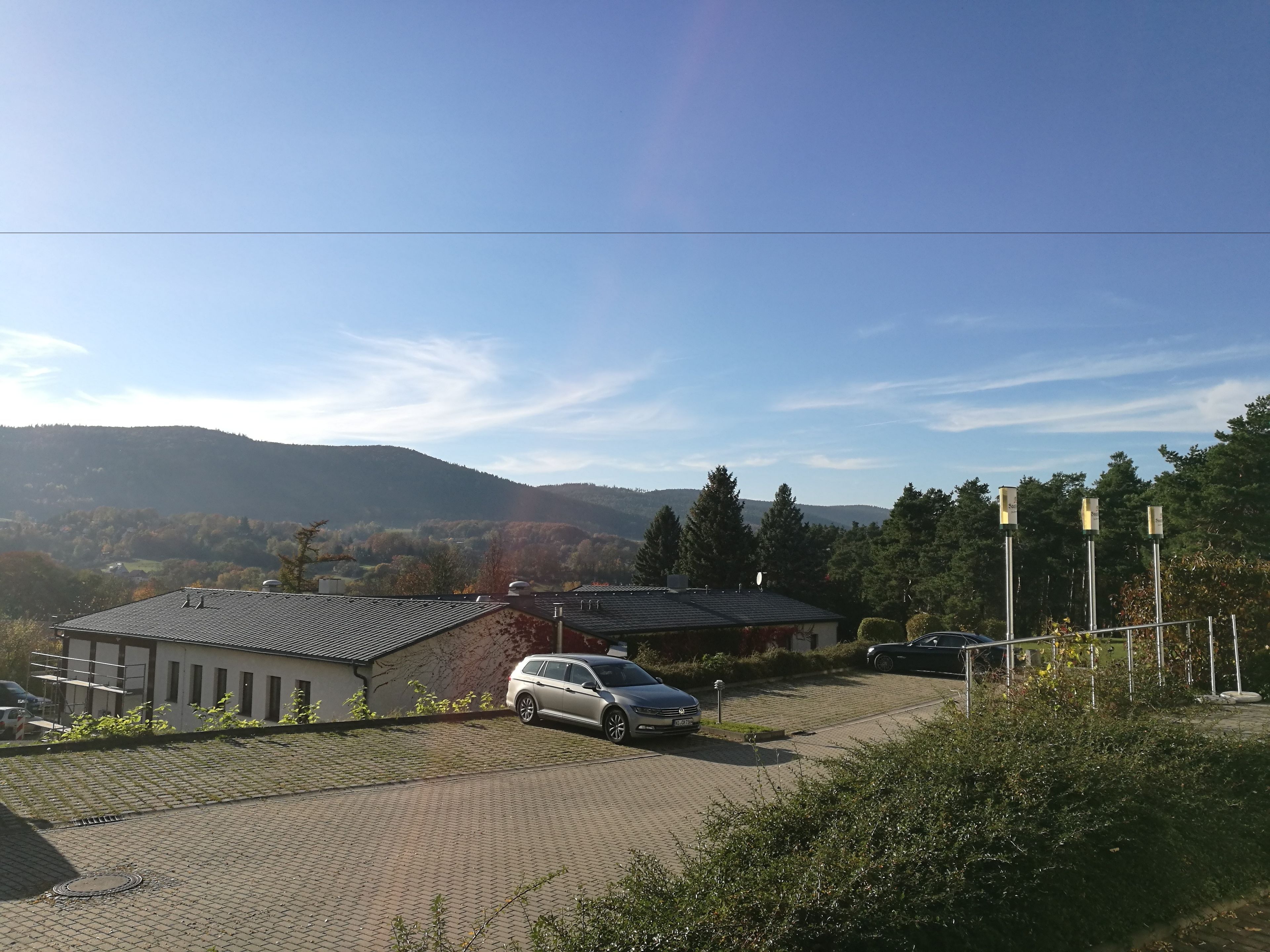 A parking area with a car, a building with a sloped roof, and a mountainous backdrop.