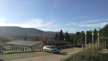 A parking area with a car, a building with a sloped roof, and a mountainous backdrop.