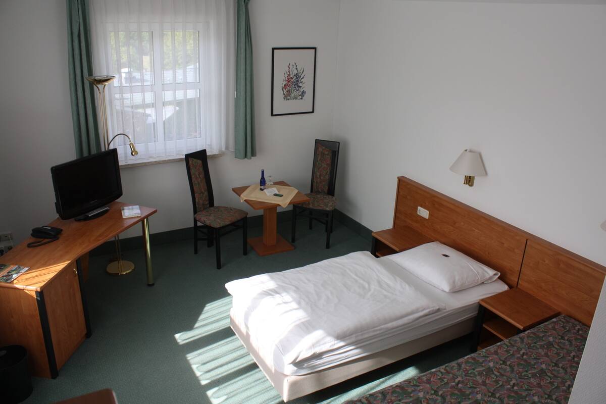 A hotel room with a bed, desk, chair, lamp, and a framed picture on the wall.