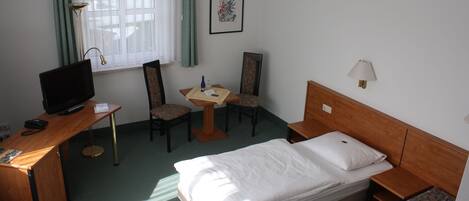 Une chambre d’hôtel avec un lit, un bureau, une chaise, une lampe et un tableau encadré au mur.