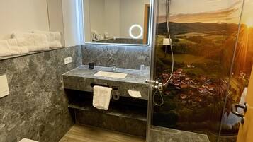 Un baño con tocador de mármol, cabina de ducha de vidrio y vistas al paisaje a través de la puerta de la ducha.