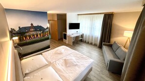 Een hotelkamer met een bed, een bureau, een stoel, een televisie en uitzicht op een gebouw door een raam.