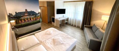 Habitación de hotel con cama, escritorio, silla, televisor y vista a un edificio a través de una ventana.
