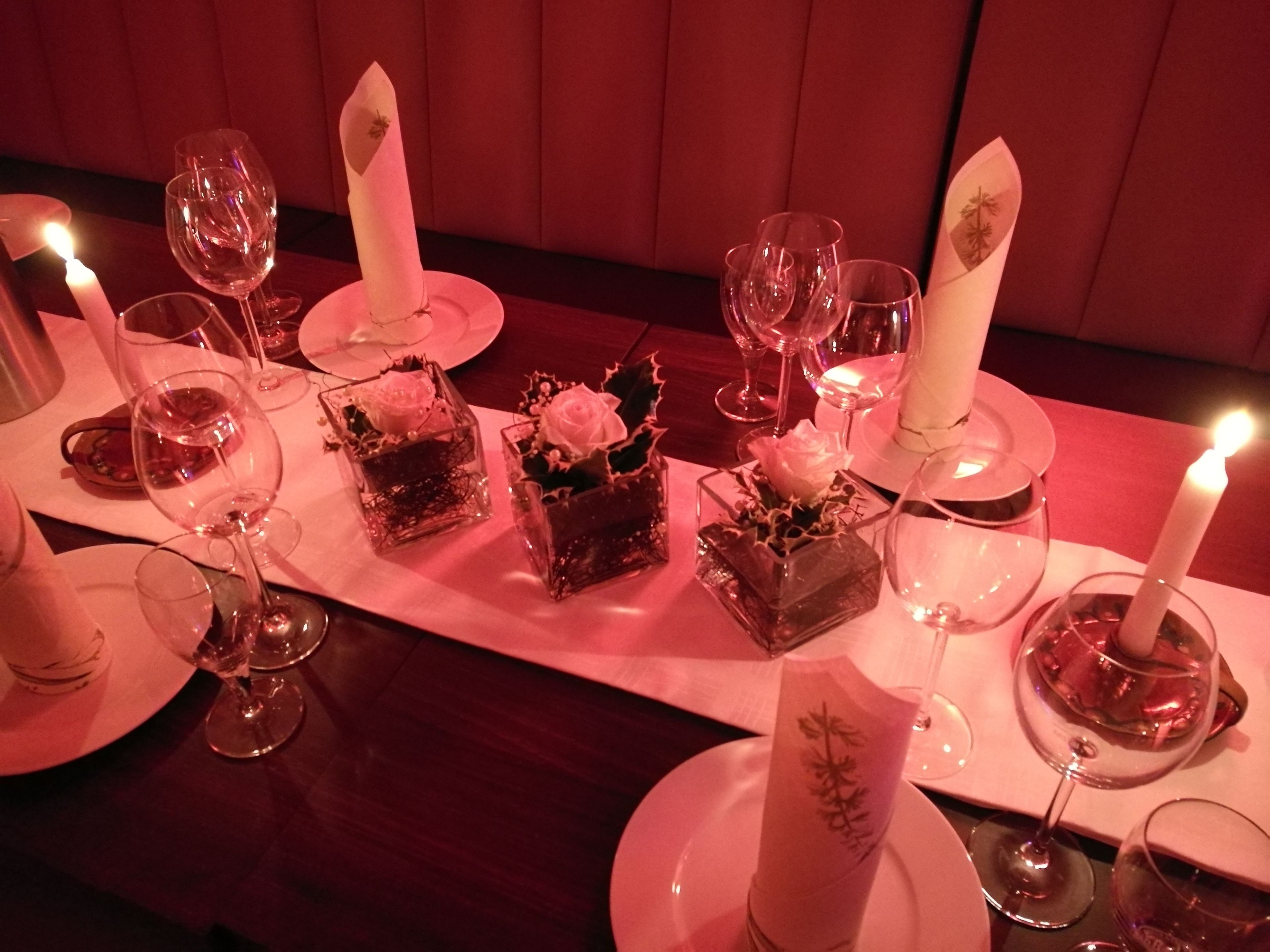 A table set for a meal with candles, wine glasses, and square dishes with flowers.