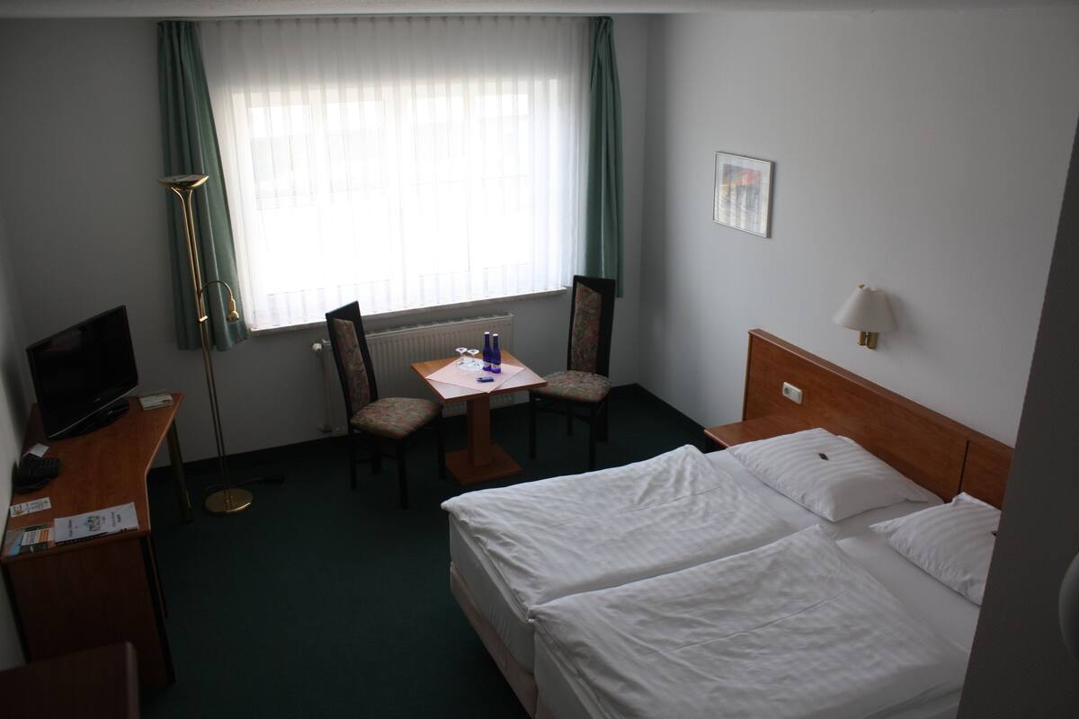 A hotel room with two beds, a desk with a chair, a TV, and a window with curtains.
