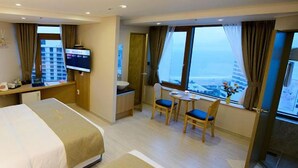 Habitación de hotel con cama, escritorio con televisor, una pequeña mesa con sillas y vistas a la ciudad.