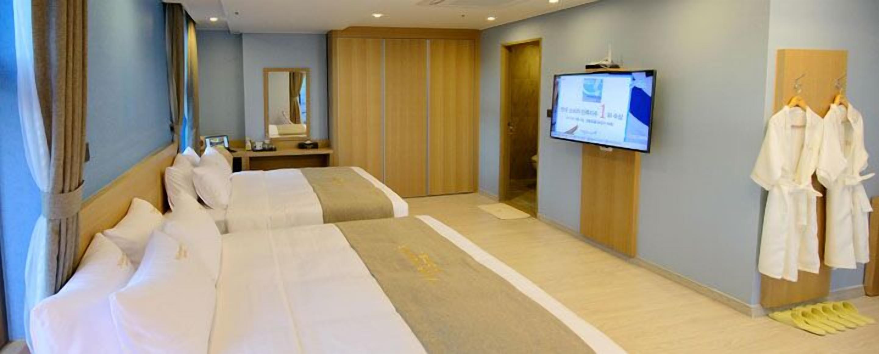 A hotel room with two beds, a TV, a mirror, and a wardrobe.