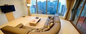 Una sala de estar moderna con un sofá en forma de L, un televisor de pantalla plana montado en la pared y un ventanal con vistas a la ciudad.
