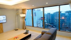 Una sala de estar moderna con un ventanal grande, un televisor de pantalla plana, un sofá y un ordenador portátil sobre una mesa de madera.