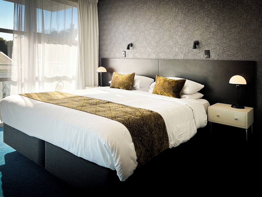 Une chambre d’hôtel moderne avec un grand lit, deux tables de chevet avec des lampes et un mur décoré d’un motif.