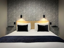 Una habitación de hotel moderna con una cama grande, dos mesitas de noche y una pared con textura.