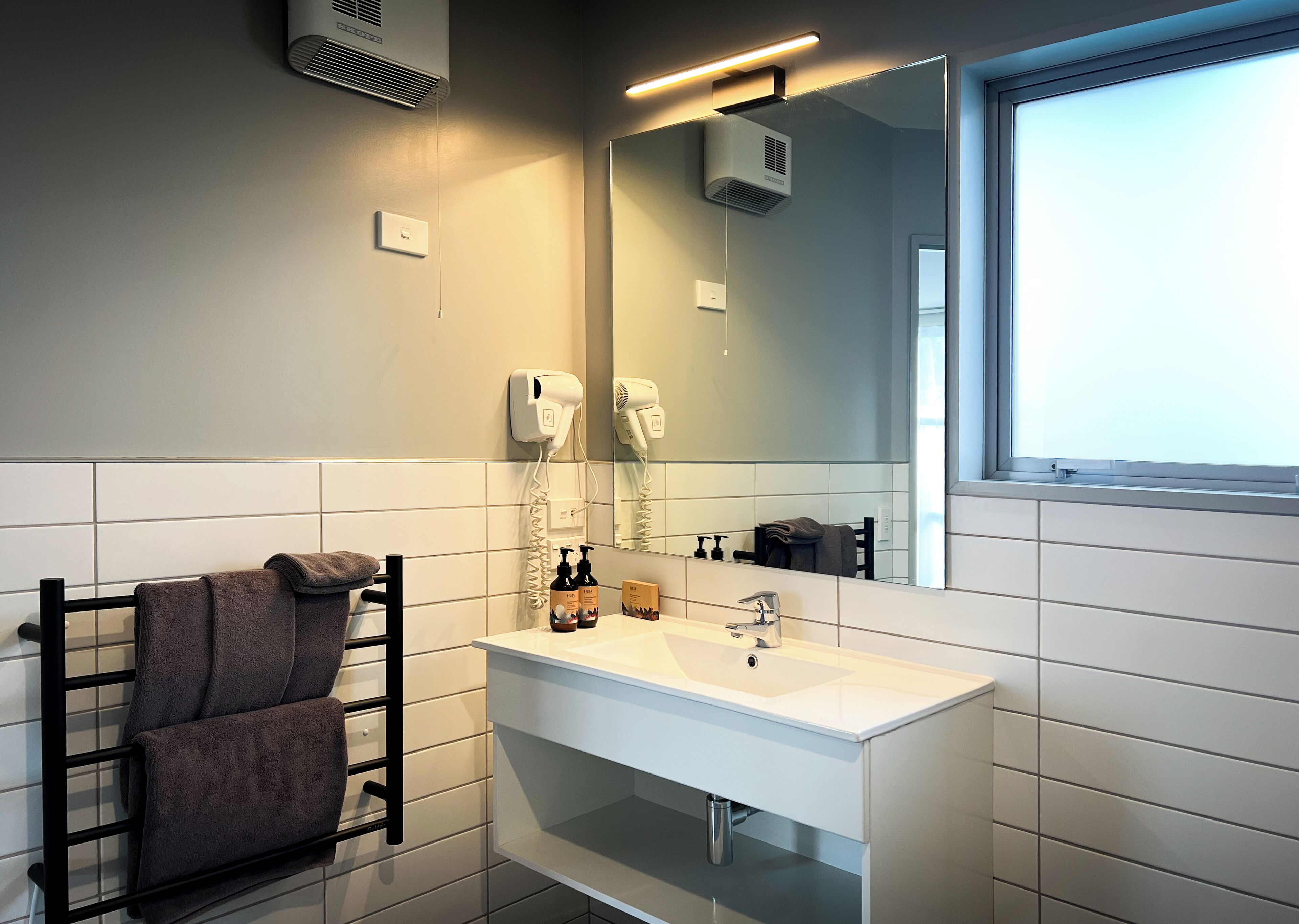 Un baño moderno con un lavabo blanco, un perchero con toallas, un secador de pelo y una ventana con vistas.
