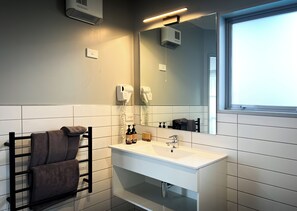 A modern bathroom with a white sink, a towel rack with towels, a hairdryer, and a window with a view.