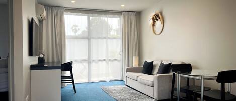 A modern, well-lit room with a blue carpet, a white sofa with black cushions, a small desk, and a chair.
