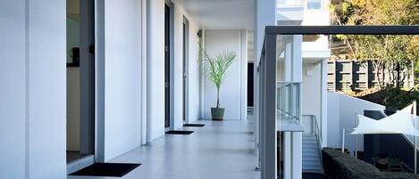 A modern, clean hallway with a potted plant, glass railing, and a view of the outside.