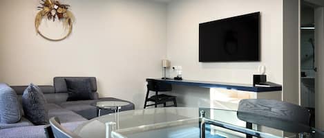 A modern living room with a glass coffee table, grey sofa, and a decorative wall piece.