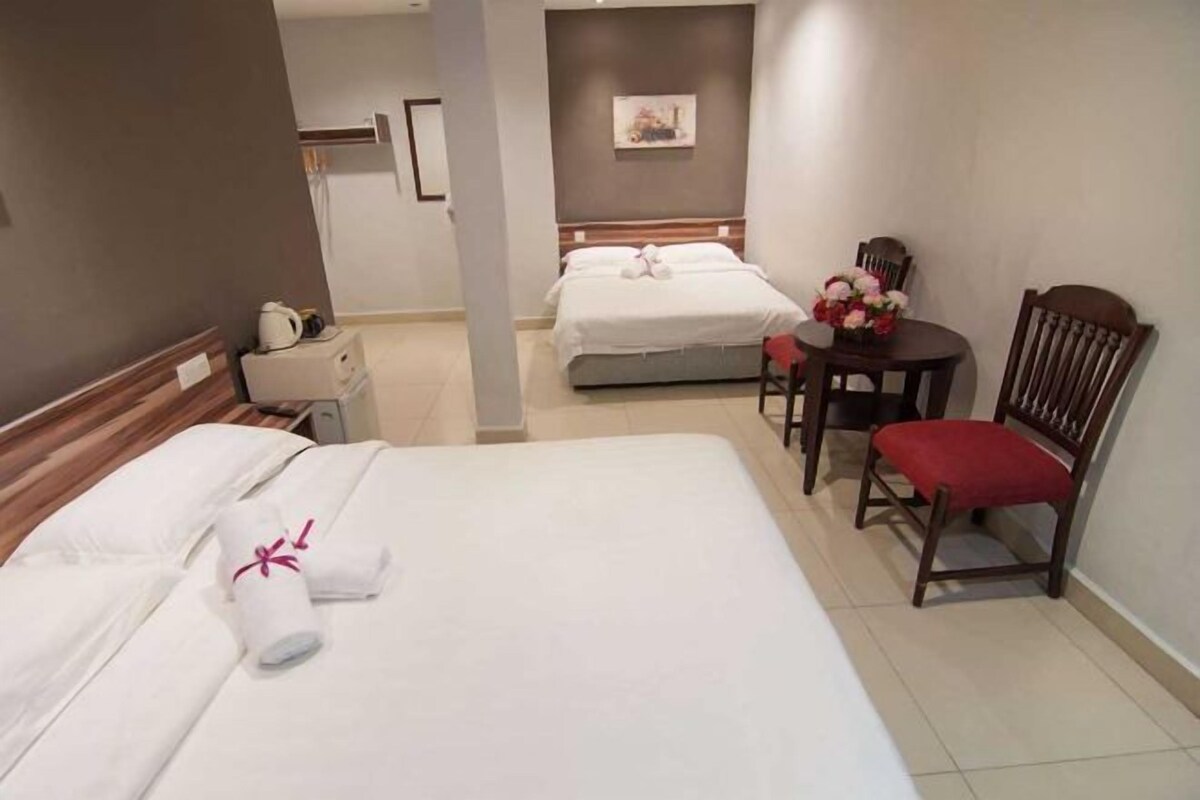 Habitación de hotel con dos camas, una mesita con un florero y una silla.