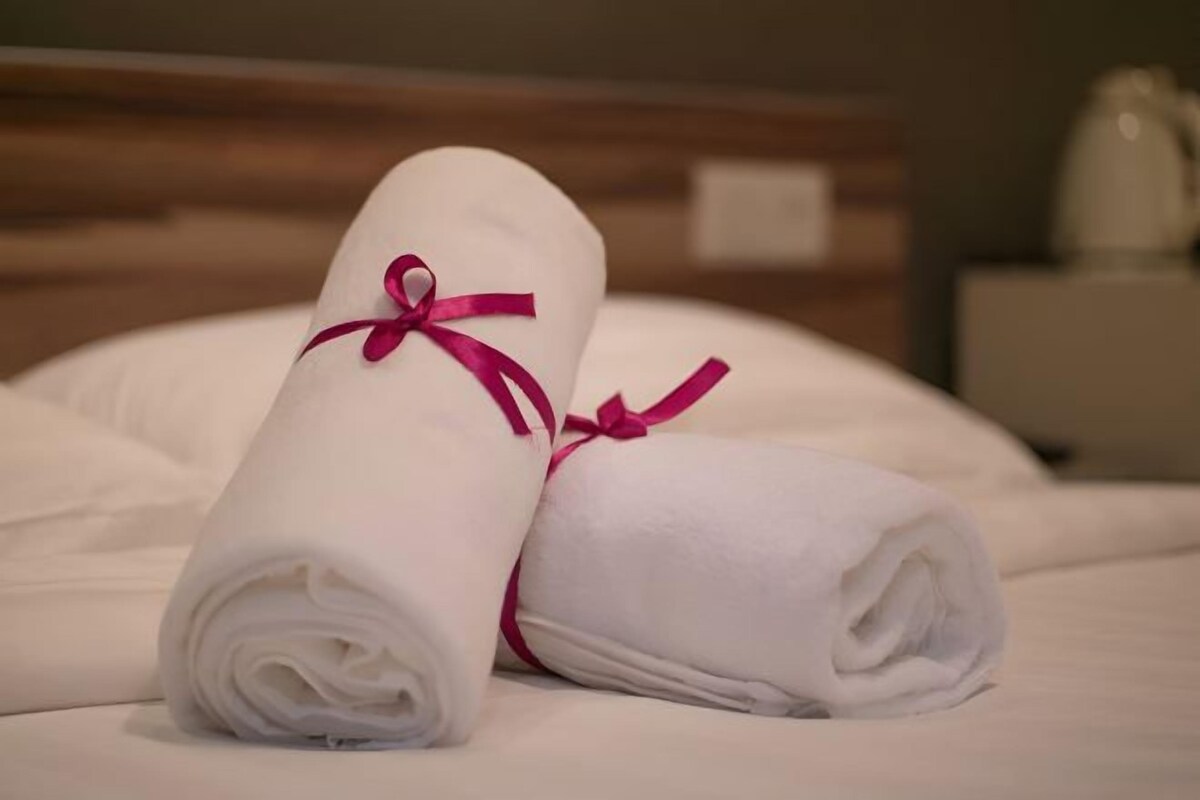 Dos toallas blancas enrolladas atadas con cintas rosas sobre una cama.