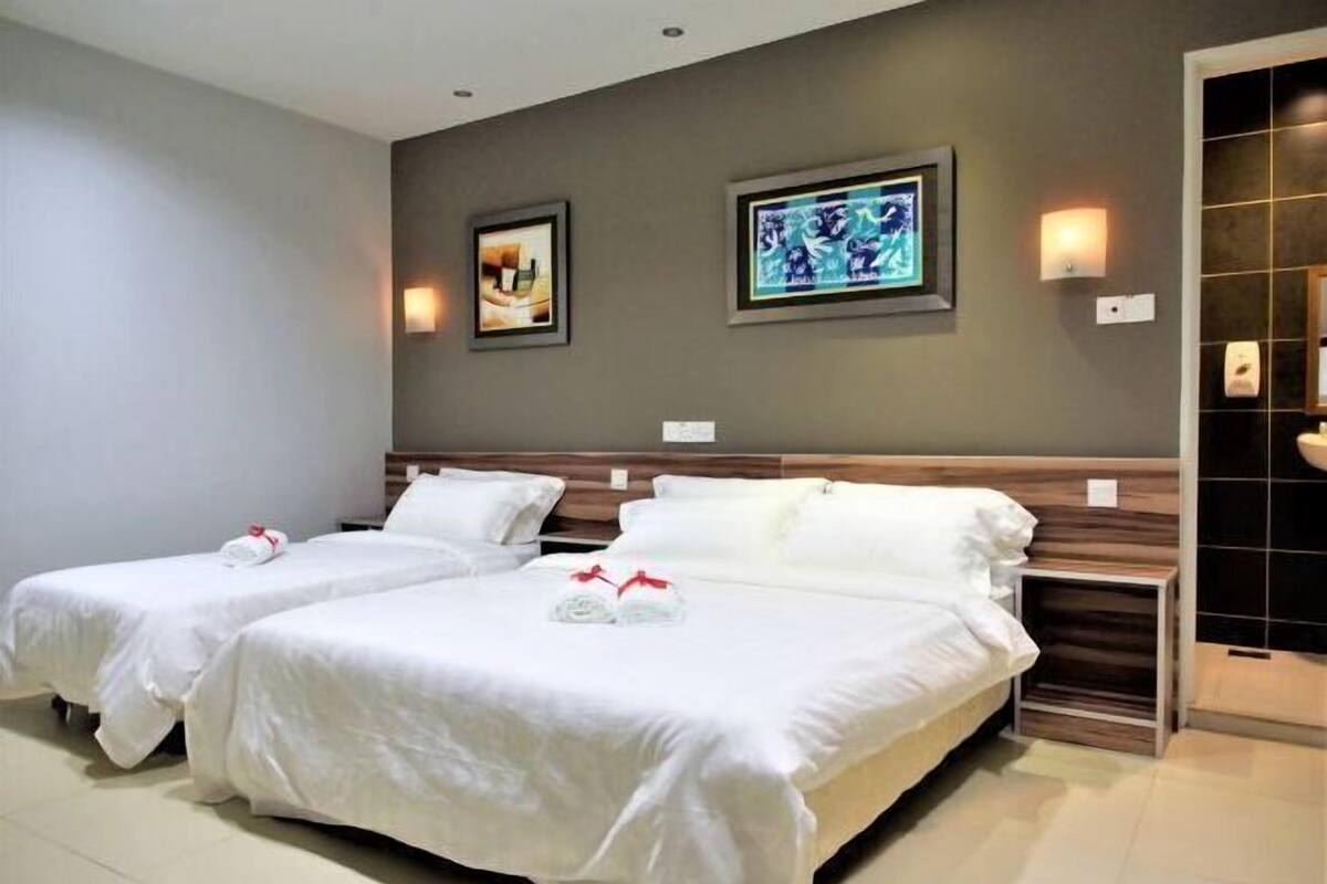 A hotel room with two single beds, a wooden headboard, and two framed pictures on the wall.