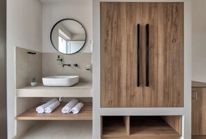 A modern bathroom with a white sink, a round mirror, and wooden cabinetry. - Zefyros Village Resort (Zakynthos)