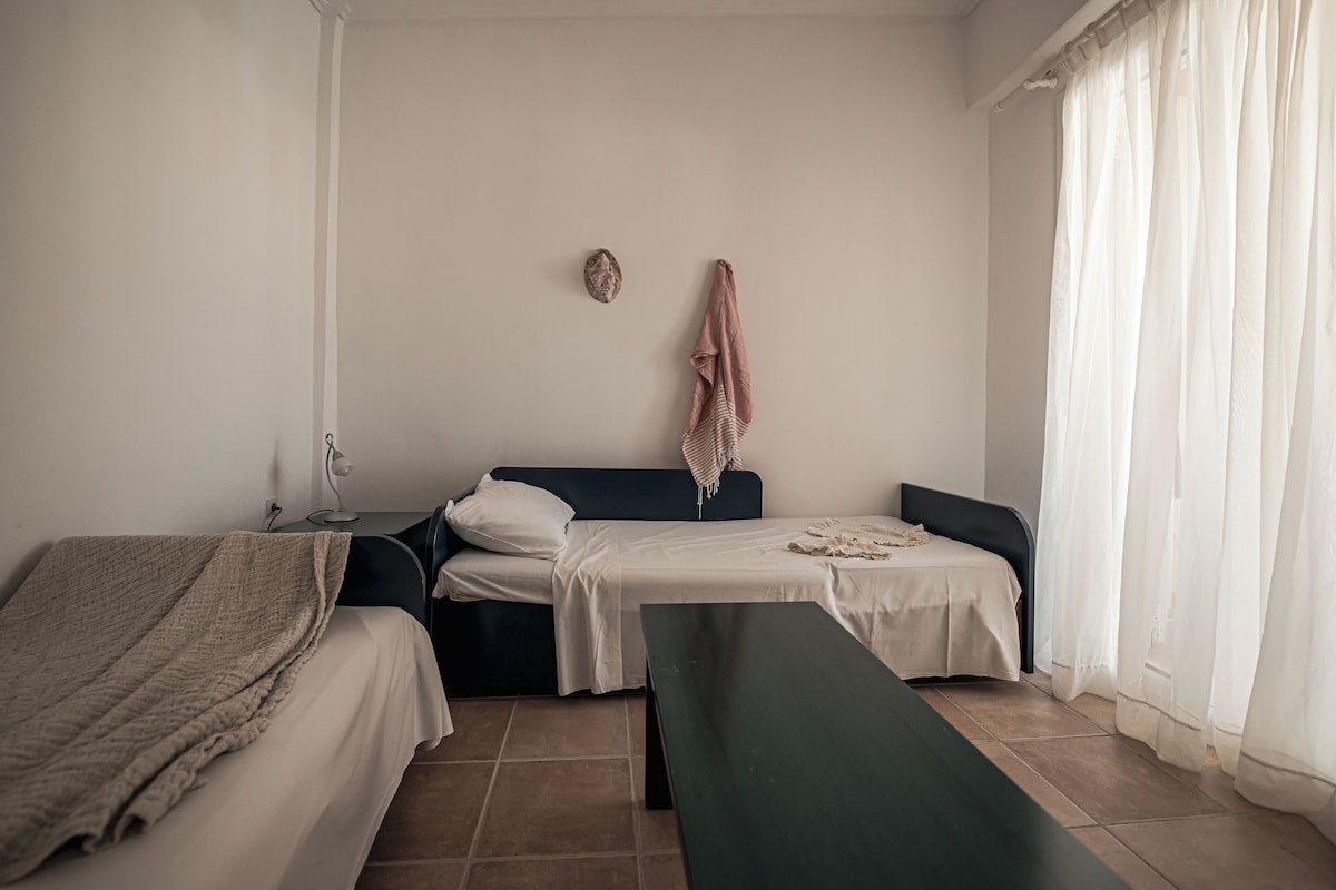 A room with two beds, a bench, a lamp, and a wall-mounted decoration.