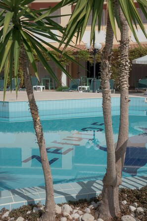 A swimming pool with tiled edges, surrounded by palm trees and lounge chairs. - Zefyros Village Resort (Zakynthos)
