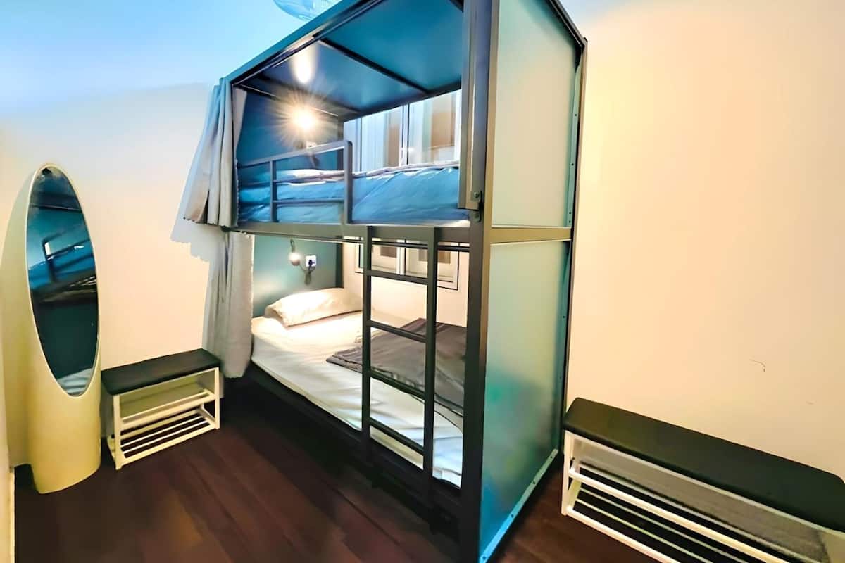 Una habitación compacta con una cama litera, una pequeña zona de estar y un espejo grande.