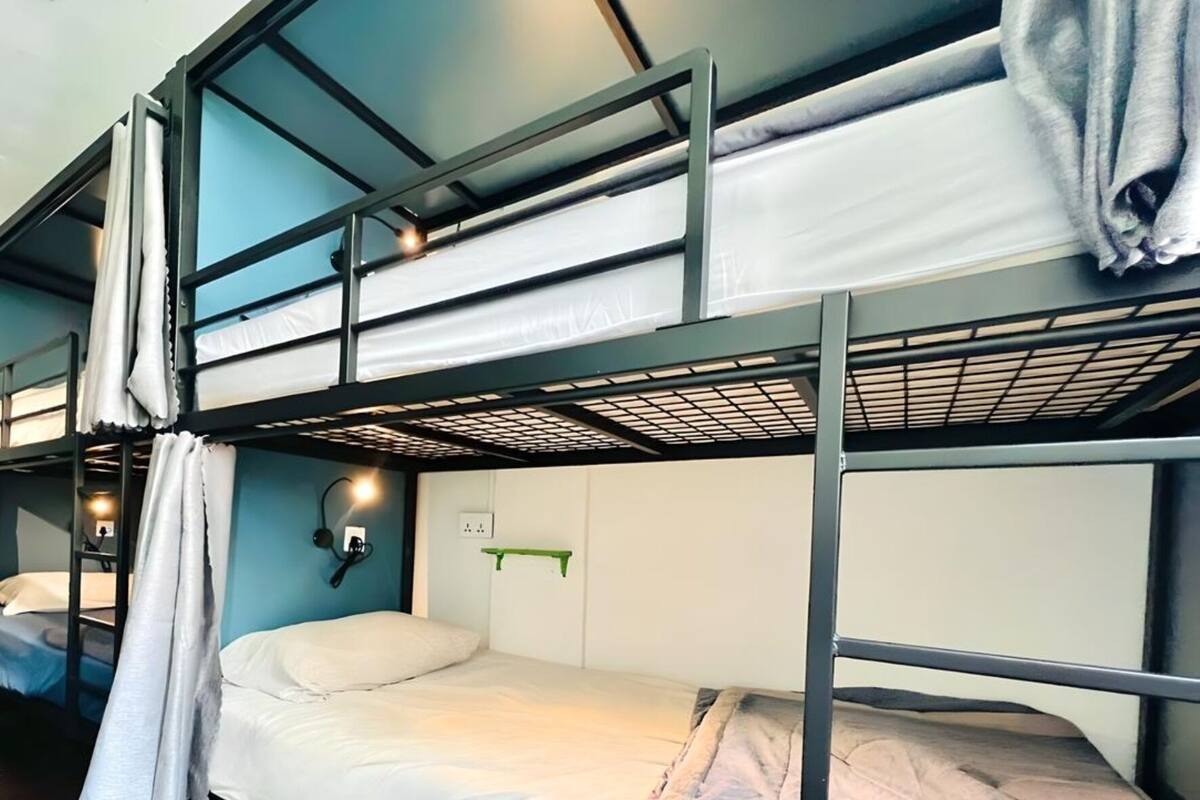 Habitación con literas, pared azul, estante verde y luz fijada a la pared.