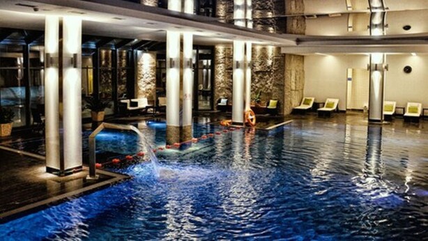 Una piscina interior con cascada, sillones de descanso y un diseño arquitectónico moderno.