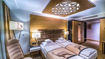 A hotel room with two beds, a wooden headboard, a modern chandelier, and a patterned carpet.