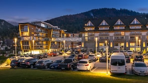 Un hotel de varios pisos con un estacionamiento lleno de coches, rodeado de montañas.