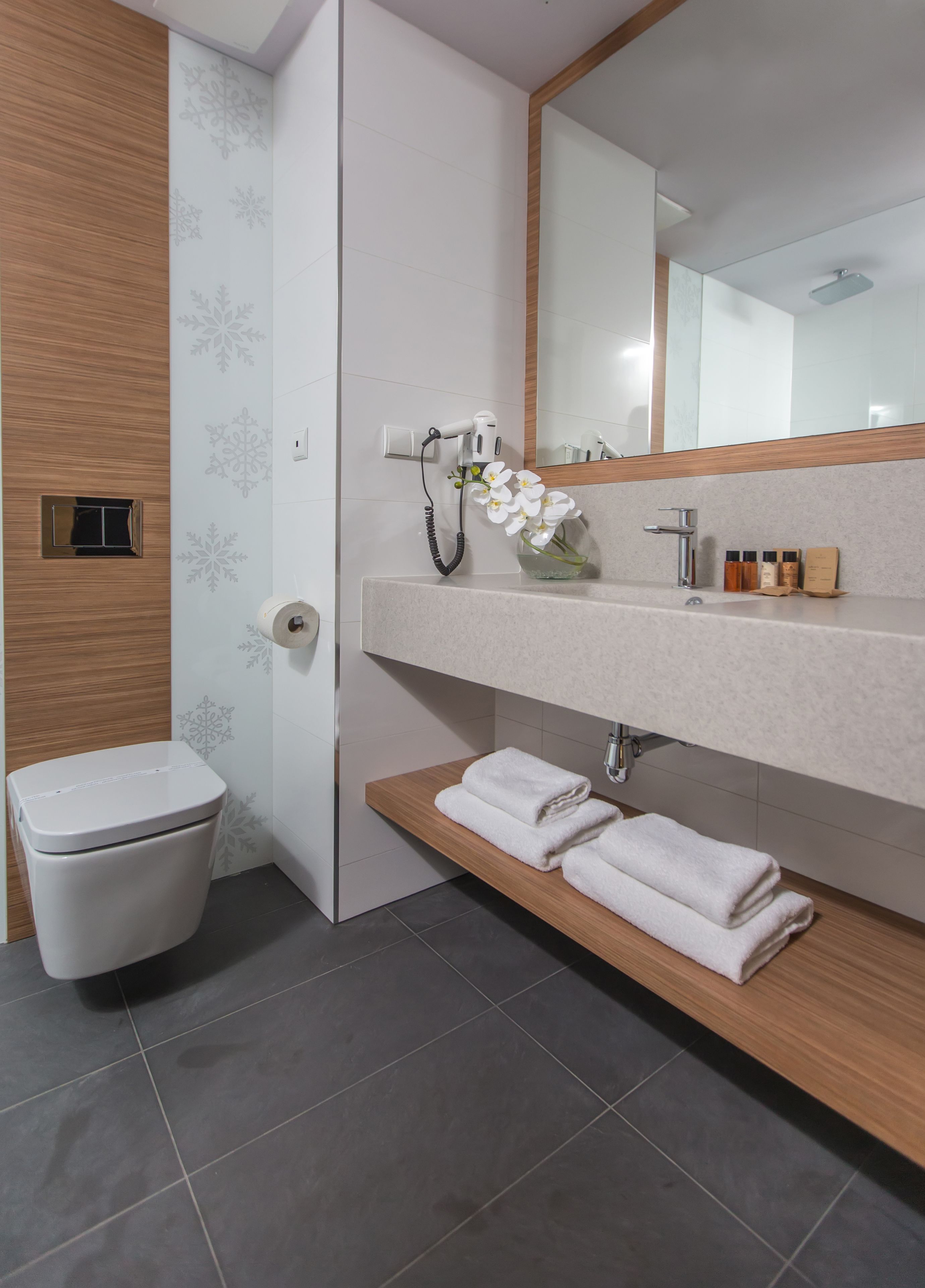 Een moderne badkamer met een toilet, een wastafel met spiegel en een plank met handdoeken.