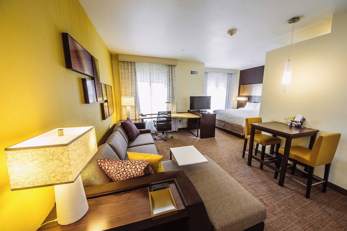 A hotel room with a sofa, a desk, a bed, a TV, and a dining table with chairs.