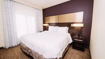 A hotel room with a large bed, a nightstand, a lamp, and a window with curtains.