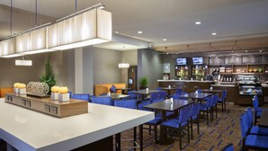 Un hall de hotel con una zona de bar, arreglos de asientos y un mostrador de recepción.