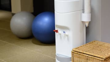 Un dispensador de agua blanco con dos grifos, una pelota de ejercicios azul y una cesta de mimbre.