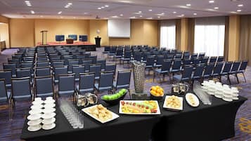 A conference room with rows of chairs, a stage, and a buffet table with various food items.