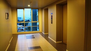 A hallway with a large window, an elevator, and a tiled floor. - Lumpini Ville Naklua Good Luck (Pattaya)