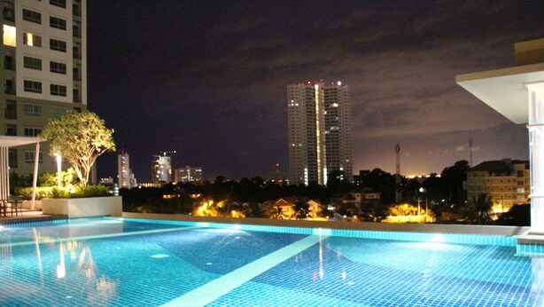 A swimming pool with a tiled edge, surrounded by buildings and a tree. - Lumpini Ville Naklua Good Luck (Pattaya)
