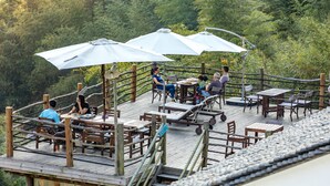 Una terraza de madera con asientos al aire libre y sombrillas, rodeada de exuberante vegetación.