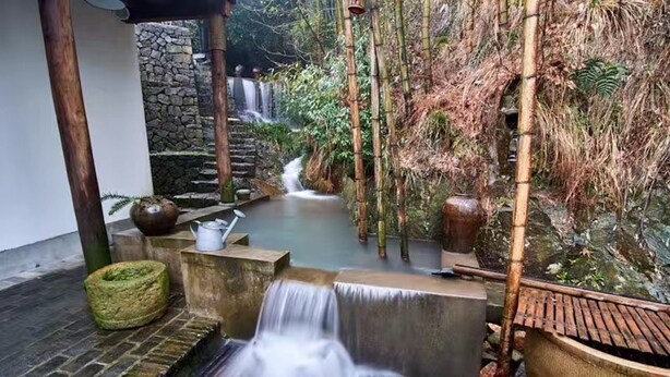 Un jardín interior tranquilo con una cascada pequeña, escaleras de piedra y estructuras de bambú.