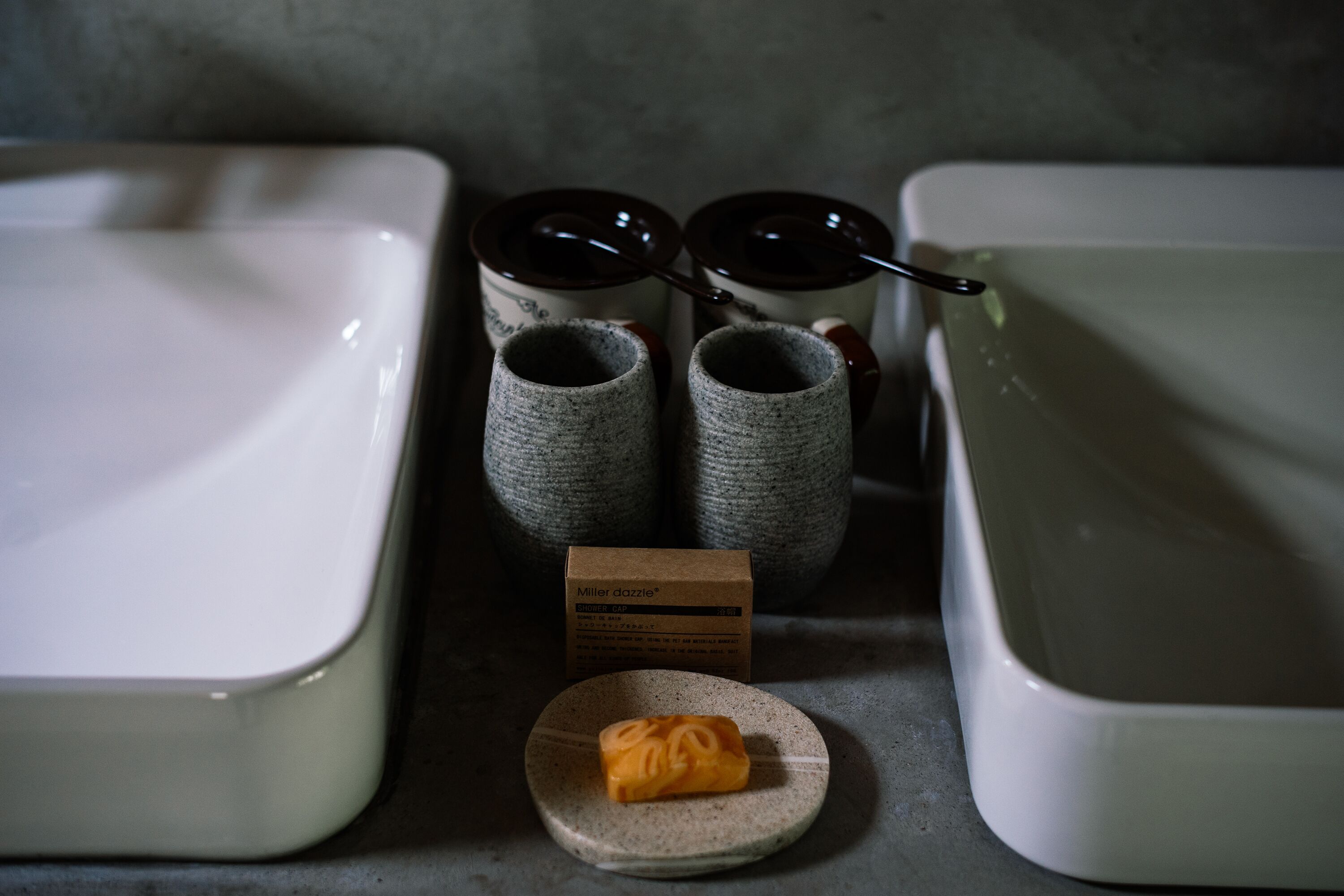Un espace cuisine comprenant deux récipients en céramique blanche, deux pots en céramique grise et une petite assiette sur laquelle se trouve un objet jaune. Une boîte en carton portant l’inscription « Miller dazzle » est également visible.