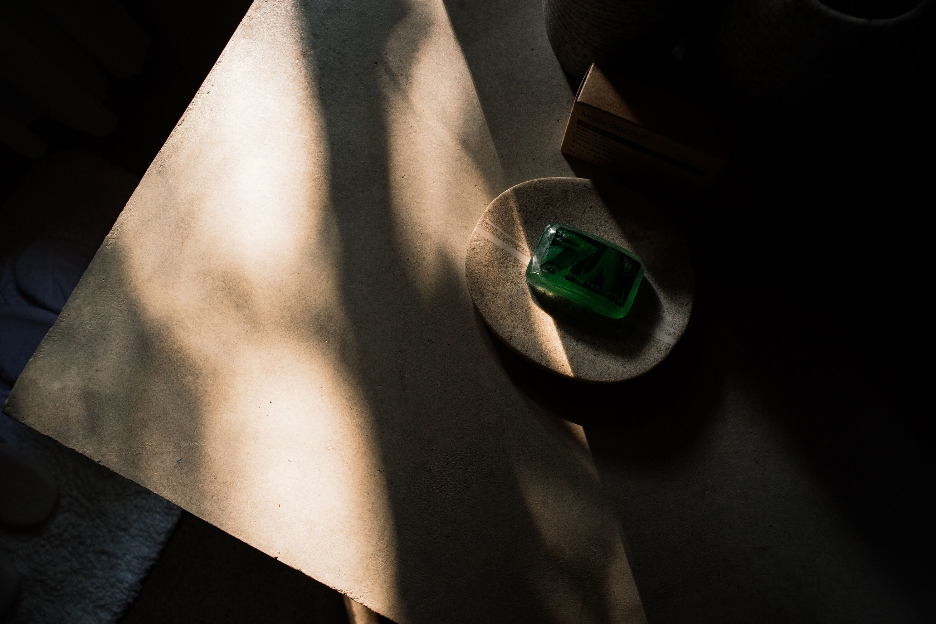 Una mesa con una botella verde y una caja, iluminada parcialmente por la luz del sol.