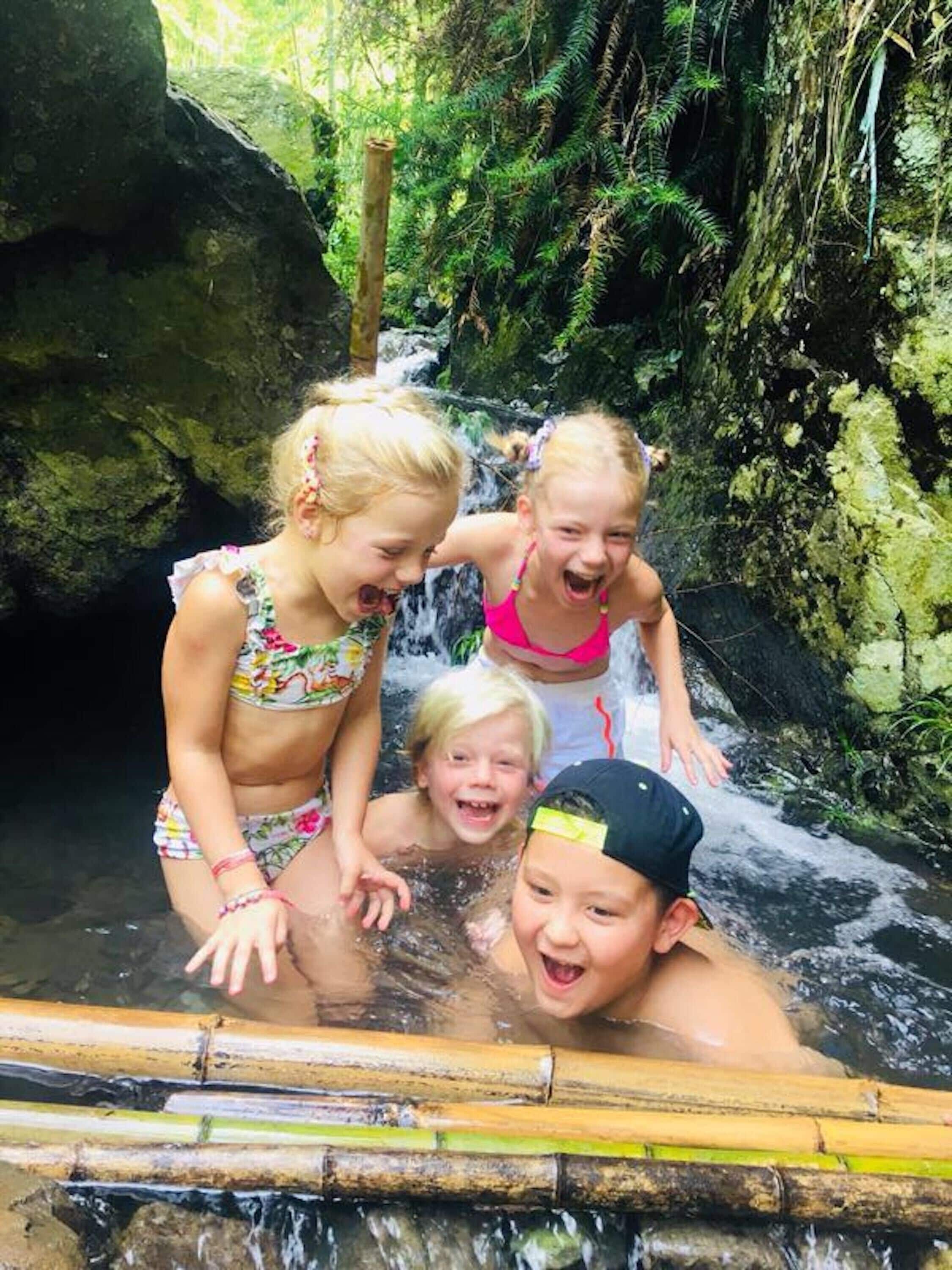 A group of children playing in a natural water feature surrounded by greenery.