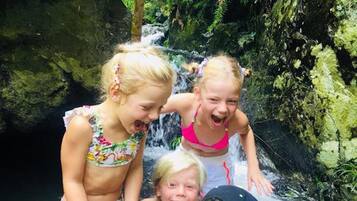 A group of children playing in a natural water feature surrounded by greenery.