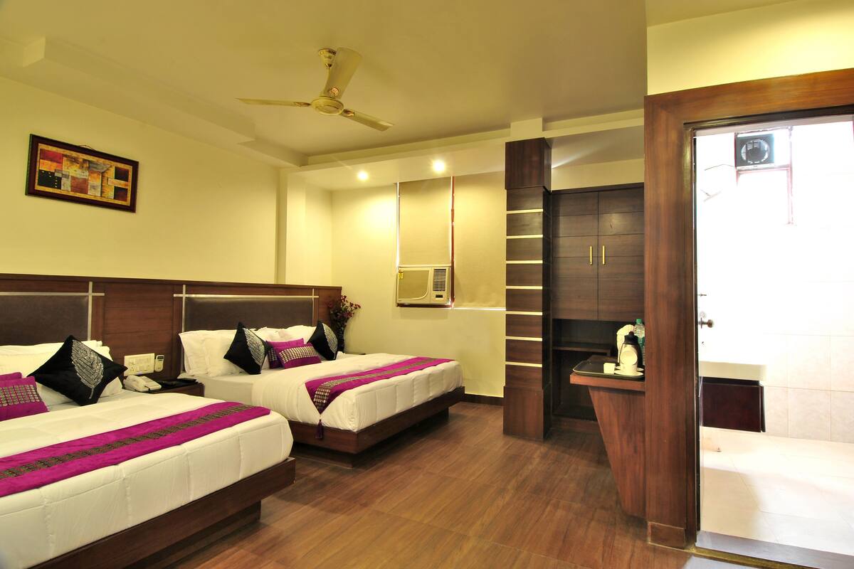 A hotel room with two beds, a ceiling fan, a minibar, and a bathroom with a bathtub.